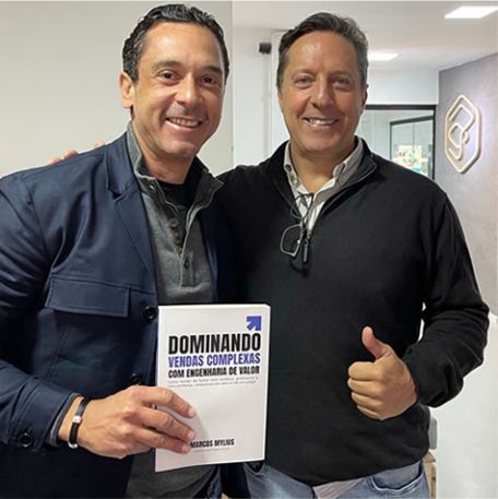 Leitor segurando o livro Dominando Vendas Complexas ao lado de Marcos Mylius