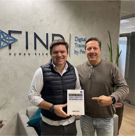 Leitor segurando o livro Dominando Vendas Complexas ao lado de Marcos Mylius