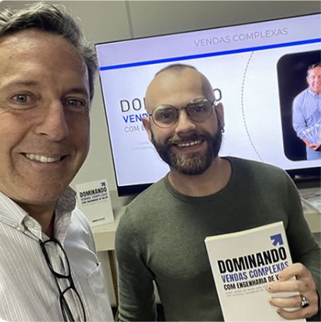 Leitor segurando o livro Dominando Vendas Complexas ao lado de Marcos Mylius
